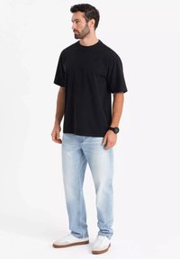 Černé tričko s krátkým rukávem, volný střih, v kombinaci s světle modrými džíny a bílými teniskami s hnědými akcenty. Hladká textura po celém povrchu.