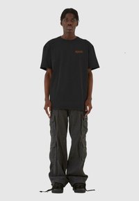 Sort bomulds T-shirt med orange logo på brystet, parret med grå cargo bukser med flere lommer og snoretræk i kanten.