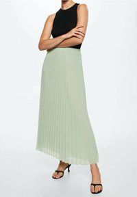 Falda midi plisada en verde claro, confeccionada en tejido fluido. Presenta una cinturilla elástica y un dobladillo ligeramente asimétrico.
