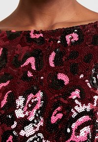 Haut en sequins bordeaux présentant un motif léopard avec des sequins noirs, roses et blancs disposés en un motif texturé et brillant.