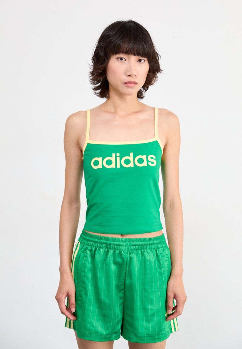 Groene tanktop met gele banden en het "adidas" logo, gecombineerd met groene gestreepte shorts. De stof lijkt glad; sportief ontwerp.