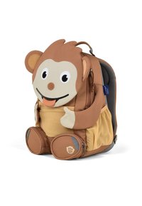 Brauner Rucksack in Form eines Affen mit großen, runden Augen, einem strukturierten Stoffkörper und einer Netzseitentasche. Die Füße besitzen kreisförmige Reißverschlusstaschen.