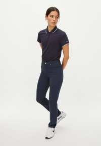 Marineblauwe polo met een contrasterende kraag en drie knopen, gecombineerd met aansluitende marineblauwe broek en witte sneakers. Eenvoudig ontwerp, soepele textuur.