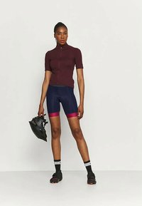 Burgundijas krāsu īsām piedurknēm šķīrējvīrs ar rāvējslēdzēju, savienots ar tumši ziliem piegulošiem šortiem ar rozā gradientu. Uzvalkots melns ķiveres un velo apavus.