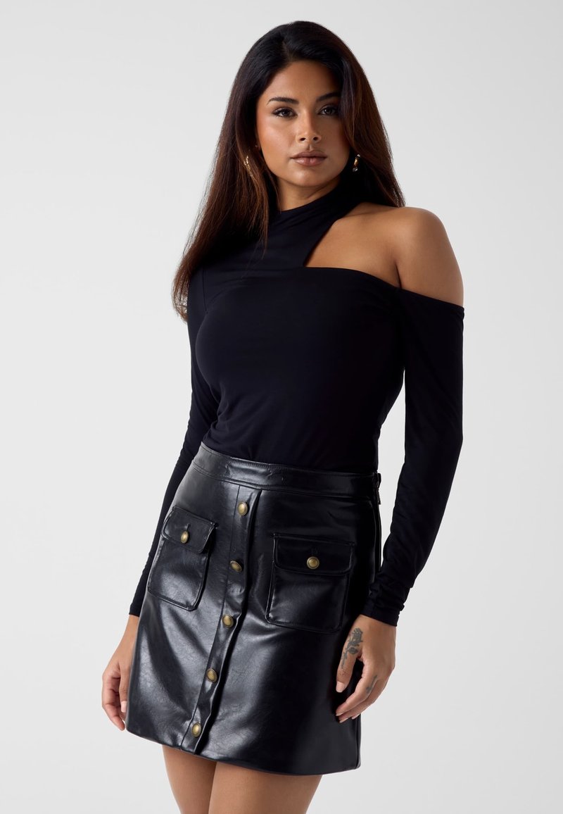 Zwart langärmelig bovenstuk met een off-shoulder ontwerp, gecombineerd met een zwarte leren rok met knopen aan de voorkant en twee opgestikte zakken.