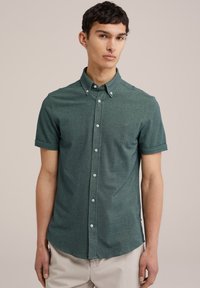 Camisa de manga corta de botonadura en tejido texturizado verde oscuro con botones blancos, que presenta un pequeño logo bordado en el pecho.