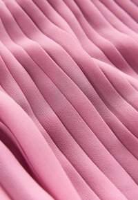 Plisseret stof i blød pink, der fremhæver vertikale teksturerede folder, lavet af letvægtsmateriale med en glat overflade.