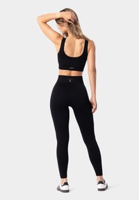 Conjunto deportivo negro que incluye una camiseta cropped y leggings de tiro alto. La tela es suave, elástica y ajustada al cuerpo. Detalle de marca mínimo.