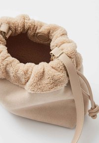 Borsa a sacchetto beige con texture morbida, chiusura con cordoncino e tracolla in pelle regolabile su sfondo bianco.