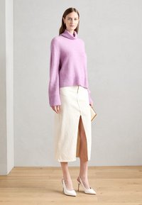 Suéter de cuello alto de punto morado, diseño ajustado, combinado con una falda midi color crema con una abertura en el frente y zapatos de tacón blanco.