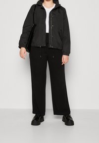 Chaqueta negra ligera con capucha, cierre frontal con cremallera y puños elásticos, combinada con pantalones anchos negros y zapatos negros gruesos.