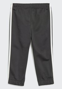Pantalons de sport noirs avec une taille élastique et des bandes blanches sur les côtés. Fabriqués dans un tissu lisse et léger, avec des poignets fuselés aux chevilles.