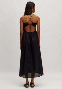 Schwarzes Maxikleid mit einem enganliegenden Oberteil, offenem Rücken und überkreuzten Spaghetti-Trägern. Mit gesammelter Taille und fließendem, leichtem Stoff.