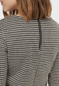 Svartvitt houndstooth-mönstrat klänning med hög halsringning och en synlig dragkedja bak. Texturerat tyg.