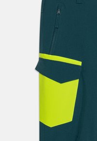 Σορτς εργασίας από σκούρο τιρκουάζ ύφασμα, με μια μεγάλη κίτρινη τσέπη και μια τσέπη με φερμουάρ. Η υφή είναι λεία με ενισχυμένες ραφές.