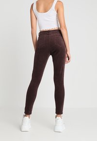 Burgunderfärgade corduroy skinny byxor med hög midja, med bakfickor och i kombination med vita sneakers. Slät textur och figurnära design.