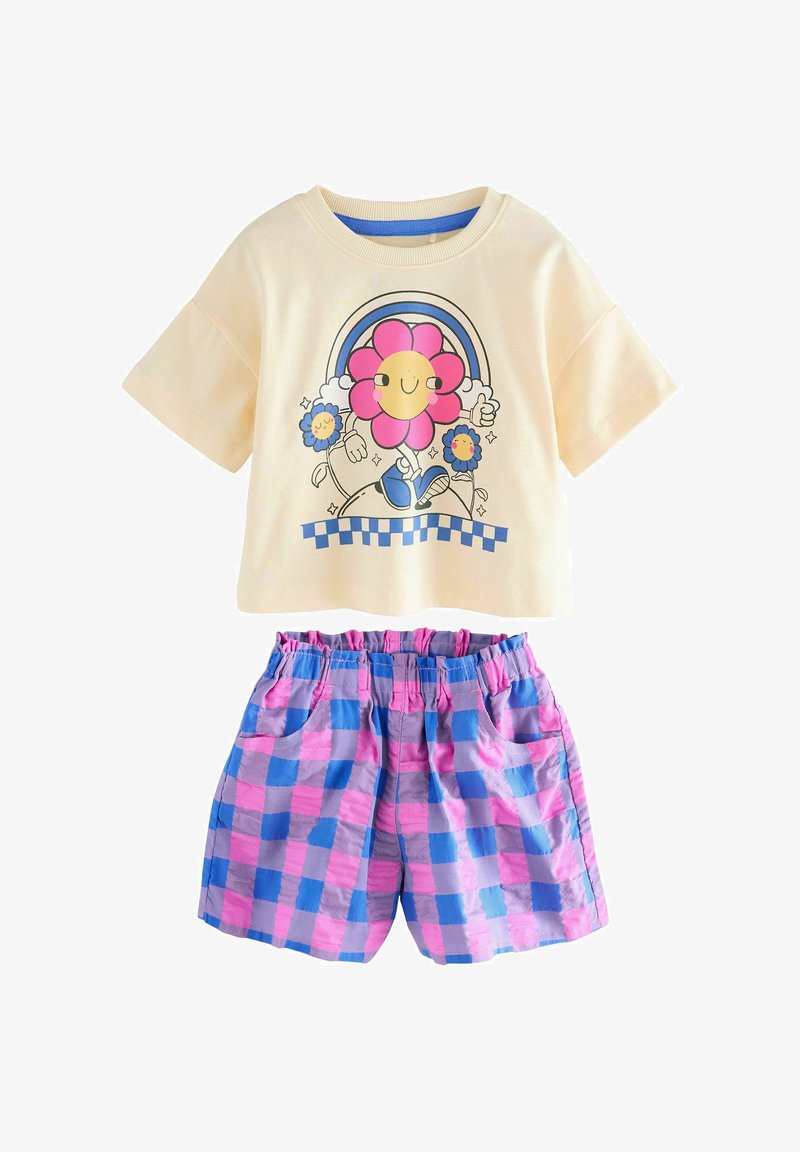 Chemise crème à manches courtes avec une fleur dessin animé souriante et un arc-en-ciel, associée à un short à taille élastique à carreaux rose et bleu.
