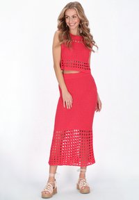 Felroze, gebreide tweedelige set met een cropped top met uitsparingen en een bijpassende midi-rok met een gestructureerde zoom. Gedomineerd door espadrille sandalen.