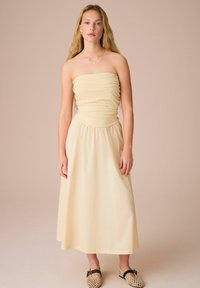 Strapless midi-jurk in zachte beige stof, met geplooide details bij de buste en taille, een vloeiende rok en een ontspannen pasvorm.