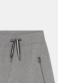 Pantalones deportivos grises con cordón en la cintura, con acentos en blanco y negro, bolsillo con cremallera lateral y tela suave y texturizada.