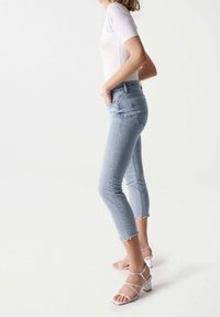 Jeans azzurri a vita alta con orlo sfilacciato e vestibilità slim, abbinati a sandali bianchi con tacco a blocco e cinturini. Tessuto denim liscio.