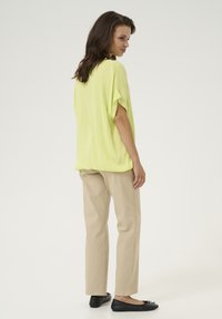 Top holgado de manga corta en un brillante amarillo, combinado con pantalones rectos beiges y bailarinas negras. Tejido texturizado con un drapeado relajado.
