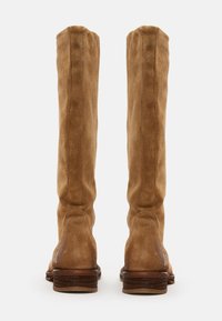 Bottes marron en daim hautes avec une texture lisse, orteil rond et talon en bois empilé, présentant des coutures discrètes le long de l'arrière.