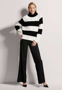 Zwart-wit gestreepte gebreide trui met een hoge hals, gecombineerd met zwarte wijde broek met krijtstrepen en puntige zwarte hakken.