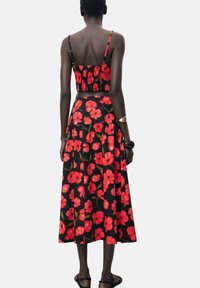 Floral two-piece set featuring a fitted crop top with thin straps and a maxi skirt, both in black fabric adorned with large red flowers.