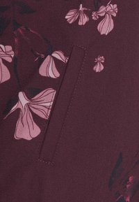 Bordeauxrode stof met een gladde textuur, versierd met roze bloemmotieven, waaronder klokvormige bloemen en stengels, met een subtiel zakdetail.