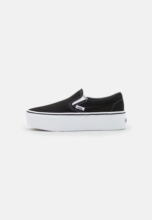 Fekete vászon slip-on cipő fehér gumitalppal, rugalmas oldalsó díszítéssel és kontrasztos varrással. Márkajelzés látható az oldalon.
