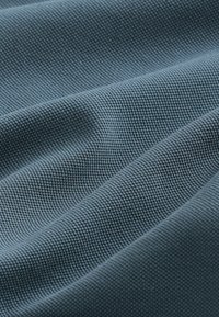 Close-up van zacht, gevouwen blauwgrijs stof met een gestructureerd, wafelachtige geweven patroon en subtiele schaduwen.