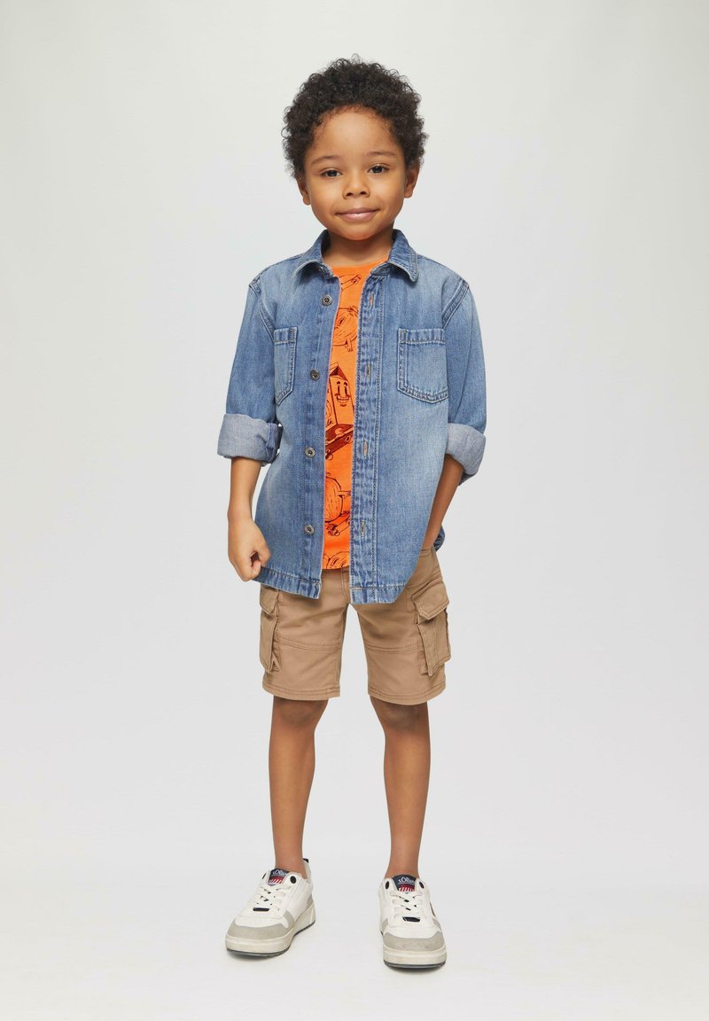 Jeanshemd mit hochgekrempelten Ärmeln über einem orangefarbenen Grafik-T-Shirt, kombiniert mit khakifarbenen Cargo-Shorts und weißen Turnschuhen.