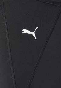 Svarta träningsleggings tillverkade av stretchmaterial, med en vit Puma-logga och platta sömmar för en elegant design.