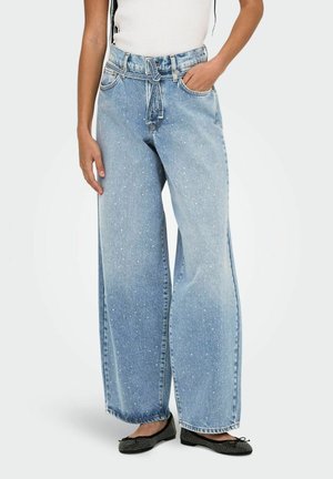 Jeans larghi di colore azzurro con un motivo a macchie, dotati di vita regolabile con cordino e tasche frontali, abbinati a scarpe nere flat.