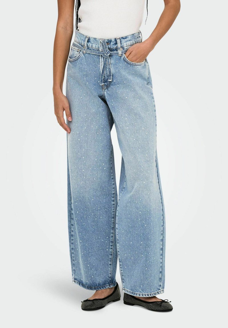 Jeans larghi di colore azzurro con un motivo a macchie, dotati di vita regolabile con cordino e tasche frontali, abbinati a scarpe nere flat.