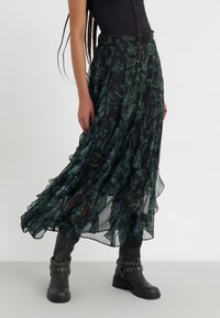 Lange, zwarte doorschijnende rok met groene bloemmotieven, gerimpelde zoom en een aangesloten tailleband. Gecombineerd met zwarte enkellaarzen met metalen accenten.
