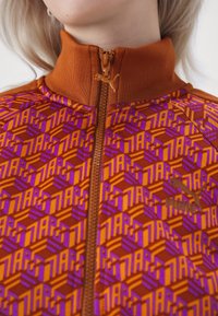 Gros plan d'un haut zippé à col montant avec des motifs géométriques orange, violet et rouge et un petit logo Puma sur la poitrine.