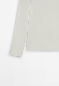 Haut long beige clair en tissu doux et lisse avec une coupe droite. Présente un col arrondi et des détails de couture minimaux.