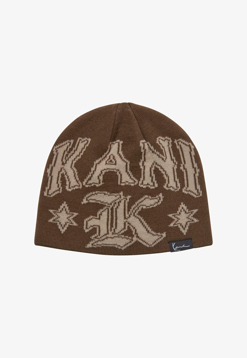 Barna kötött sapka, nagy bézs színű "KANI" felirattal és díszes csillagmintákkal. Fekete címkével rendelkezik, amely az aláírás részleteit tartalmazza.