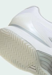 Białe buty sportowe z teksturowaną siateczkową cholewką i gładkimi plastikowymi akcentami. Gumowa podeszwa ma wzór w jodełkę dla lepszej przyczepności.
