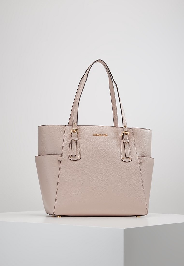 Sac fourre-tout en cuir beige Michael Kors avec double poignées, quincaillerie dorée et poches latérales, présenté sur une surface blanche.