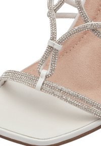 Sandal con tacco bianco caratterizzato da cinturini incrociati decorati con strass argentati. Materiale superiore liscio con una soletta morbida e texturizzata.