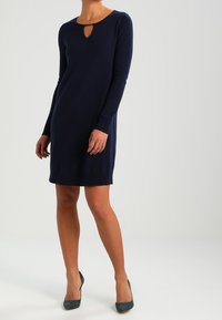 Robe longue à manches longues bleu marine avec un col rond et un détail en forme de clé. Fabriquée en tissu doux, design ajusté, longueur jusqu'aux genoux.
