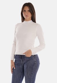 Maglione a collo alto bianco a maniche lunghe realizzato in tessuto liscio, design aderente, abbinato a jeans slim-fit blu scuro.