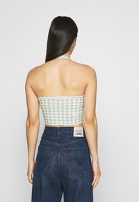 Top cropped em xadrez verde e branco com decote halter, combinado com jeans de cintura alta em denim azul que apresentam um patch com logo nas costas e detalhes em costura.