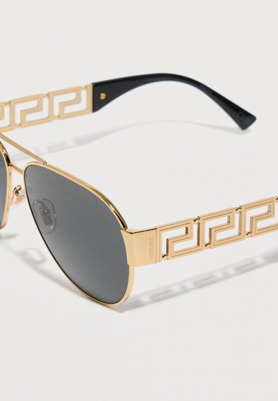 Γυαλιά ηλίου με χρυσό μεταλλικό πλαίσιο, σκούρους φακούς και ανοιχτό μοτίβο ελληνικού κλειδιού στα μπράτσα, με το χαραγμένο λογότυπο Versace στη άρθρωση.