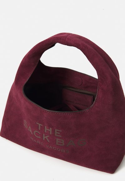 Burgundin värinen mokkanahkainen käsilaukku, jossa on pyöreä kahva. Edessä on kohokuvioitu teksti "THE SACK BAG MARC JACOBS" ja pehmeä, teksturoitu pinta.