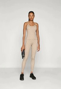 Beige sportssett med mønstrede tanktop og leggings, med en tettsittende design og åndbart materiale. Tilbehøret inkluderer en svart vannflaske.