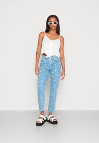 Top de linho branco cropped com detalhe em laço, jeans azul claro com bolinhas brancas e sandálias de plataforma pretas com tiras brancas.